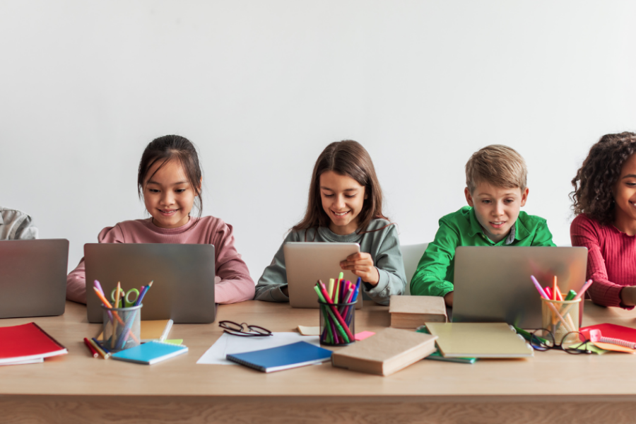 cinque bambini davanti a computer portatili seduti ad un tavolo. Gestione del patrimonio scolastico