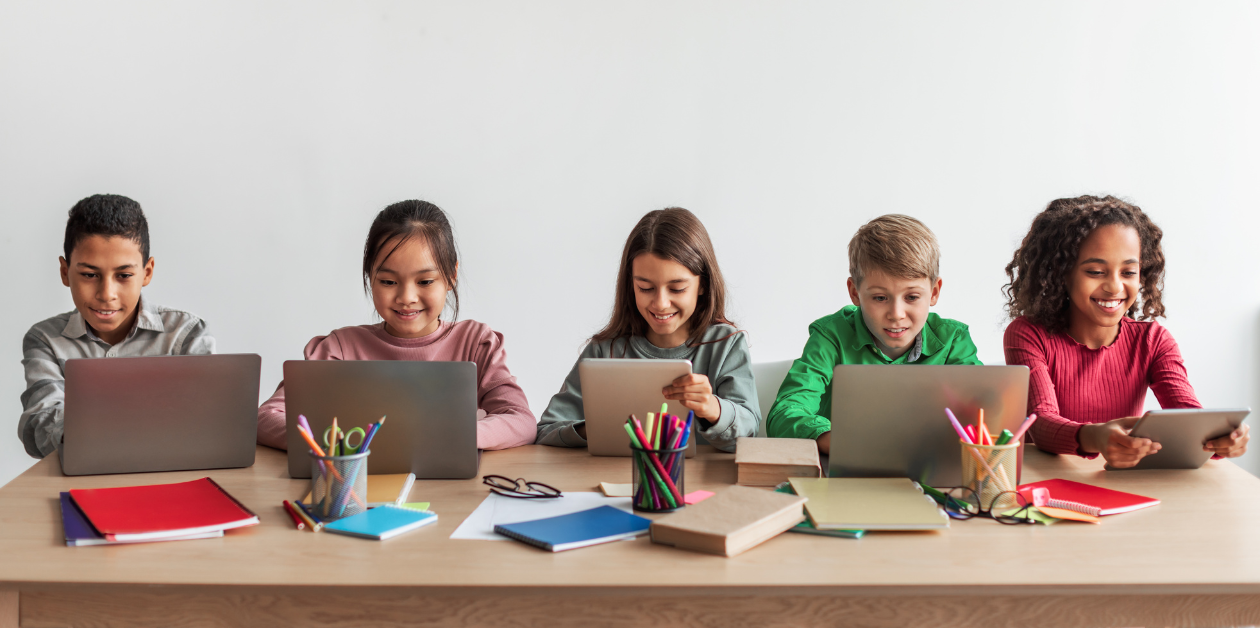 cinque bambini davanti a computer portatili seduti ad un tavolo. Gestione del patrimonio scolastico